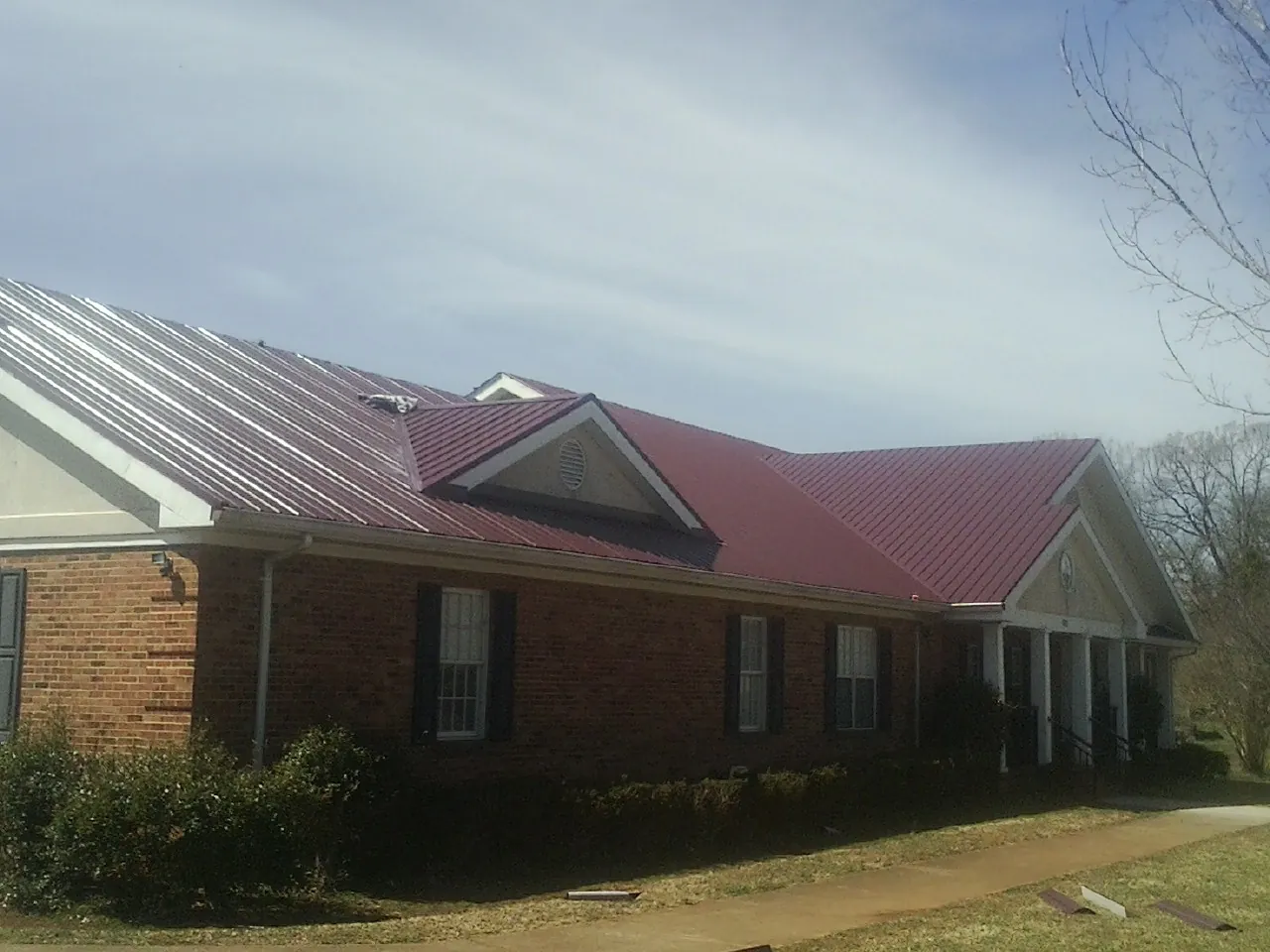 Red metal roof with gabled entries on a long brick building, from a Hail Damage Roof Repair job in Richfield