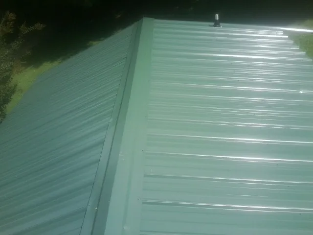 New green metal panels meeting at the ridge of a roof — Flat Roof Repair work by our crew in Richfield