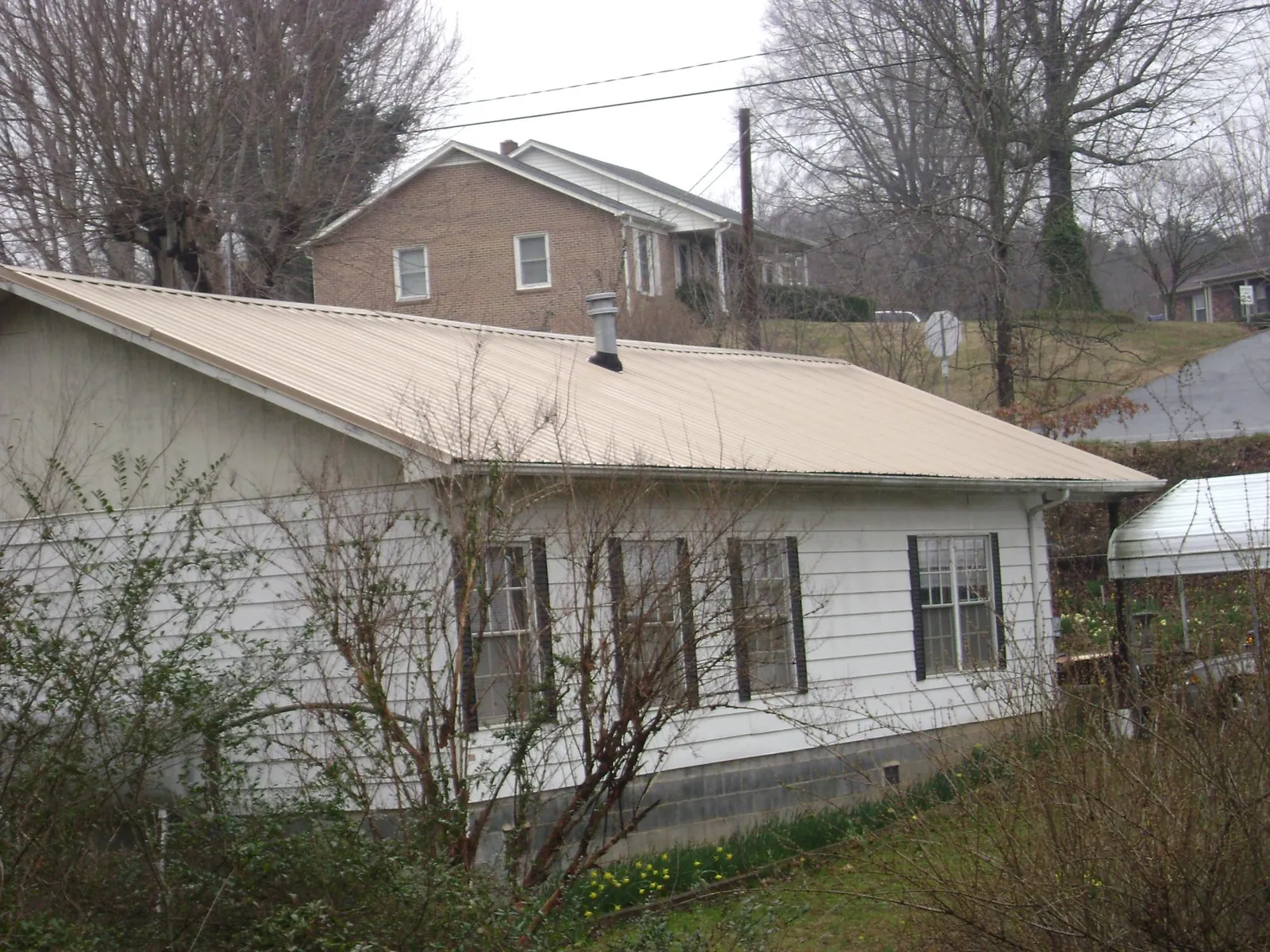 Tan metal roof on a white sided house set into a hillside — Commercial Roofing by Roofing Brothers in Richfield